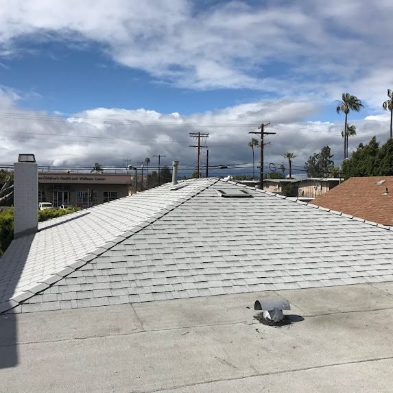 Ridge and chimney detail on a new shingle roof under cloudy skies